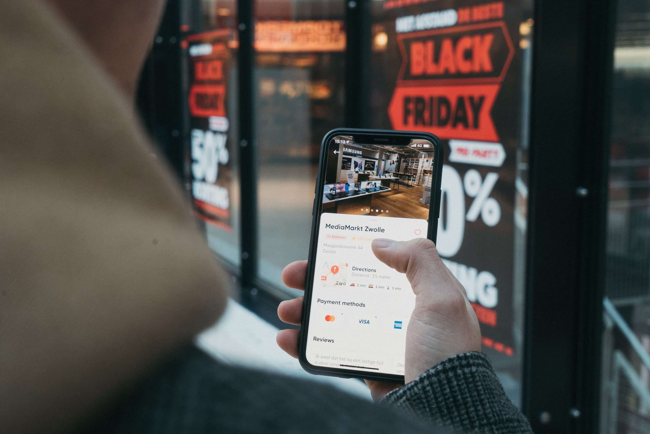 man shopping on mobile phone in front of shop window display with "black friday sale"